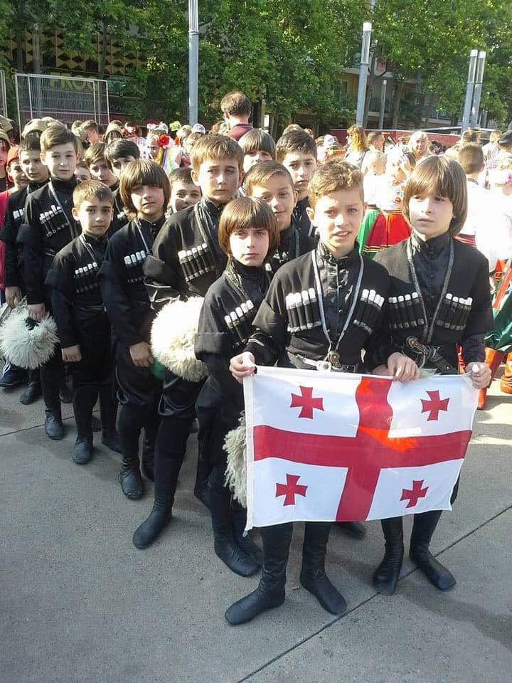 Group of young Georgian dancers in traditional costumes holding the Georgian flag